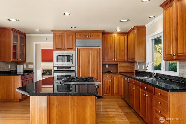 kitchen with a center island, built in appliances, crown molding, light wood-style floors, and a sink