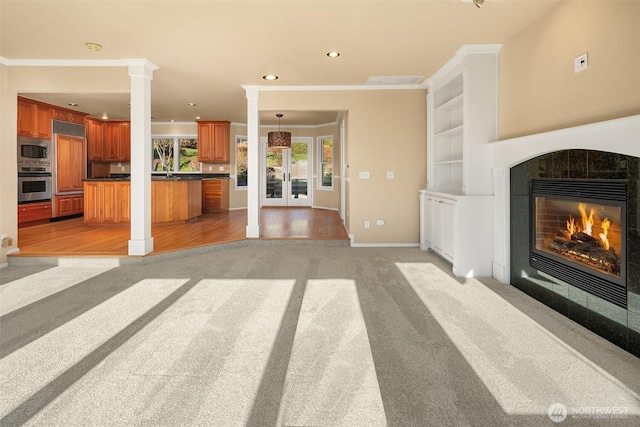 living area featuring crown molding, light colored carpet, a fireplace, and decorative columns