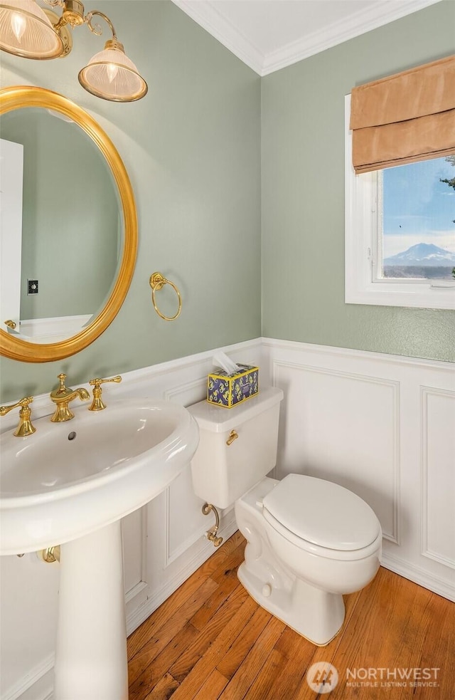 bathroom featuring a wainscoted wall, wood finished floors, toilet, and crown molding