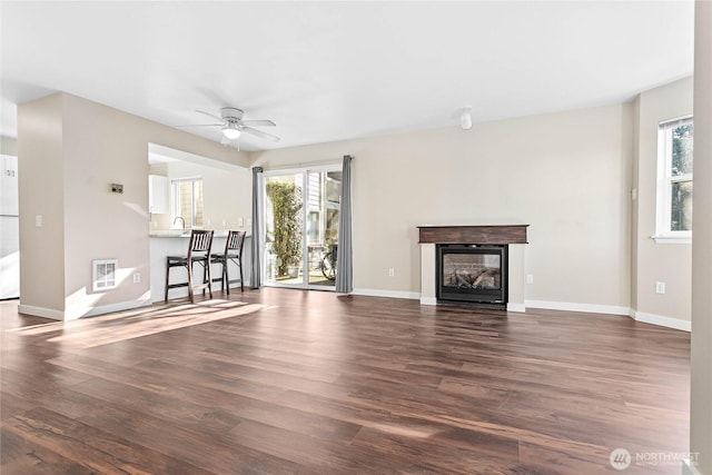 unfurnished living room with ceiling fan, a healthy amount of sunlight, dark hardwood / wood-style flooring, and heating unit