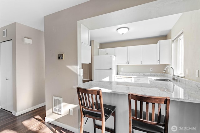 kitchen with a kitchen bar, sink, white cabinetry, kitchen peninsula, and white fridge