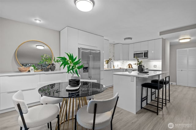 kitchen featuring tasteful backsplash, stainless steel appliances, light hardwood / wood-style floors, a kitchen island, and white cabinetry