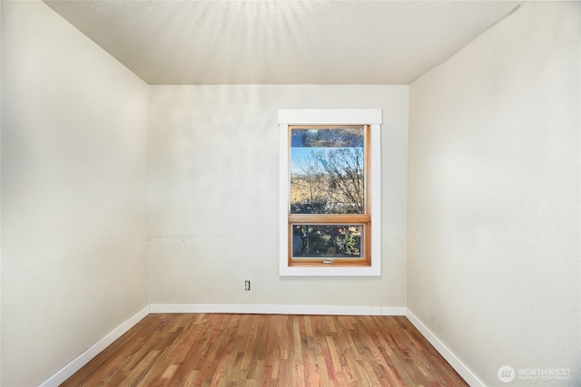 spare room with baseboards and wood finished floors