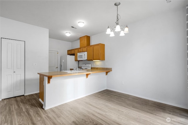 kitchen featuring white appliances, a breakfast bar, hanging light fixtures, kitchen peninsula, and light wood-type flooring