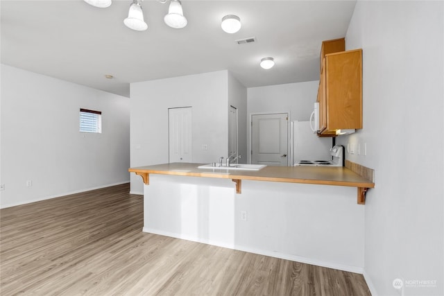 kitchen with sink, a breakfast bar area, light wood-type flooring, kitchen peninsula, and stove