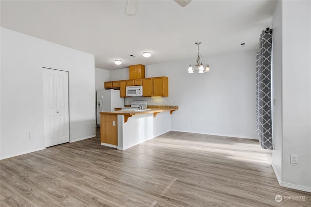 kitchen featuring decorative light fixtures, a kitchen bar, a notable chandelier, kitchen peninsula, and white appliances