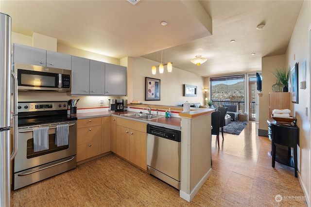 kitchen featuring appliances with stainless steel finishes, light brown cabinetry, sink, hanging light fixtures, and kitchen peninsula