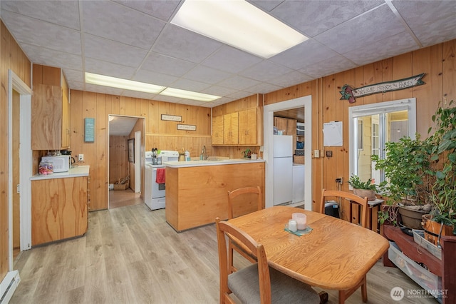 dining area featuring baseboard heating, wood walls, and light wood-style flooring