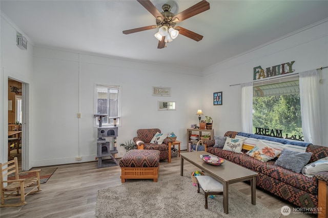 living room featuring wood finished floors, visible vents, a ceiling fan, ornamental molding, and baseboards