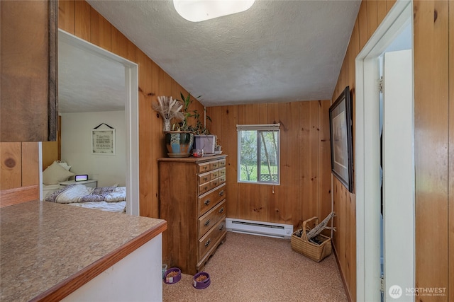 hall with a baseboard heating unit, wooden walls, a textured ceiling, and light colored carpet
