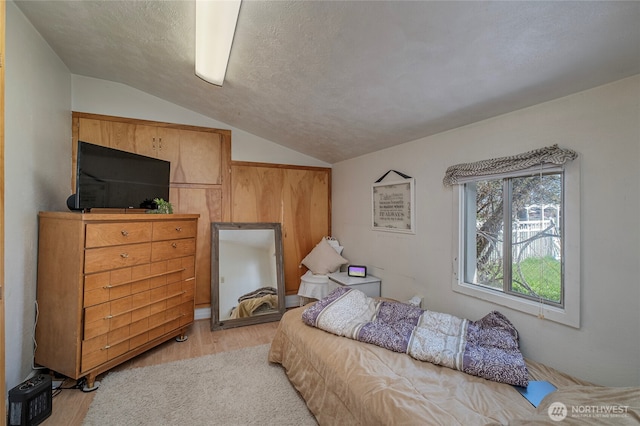 bedroom featuring light wood finished floors, vaulted ceiling, and a textured ceiling