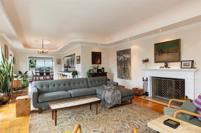 living room with an inviting chandelier, ornamental molding, a tray ceiling, and light parquet floors