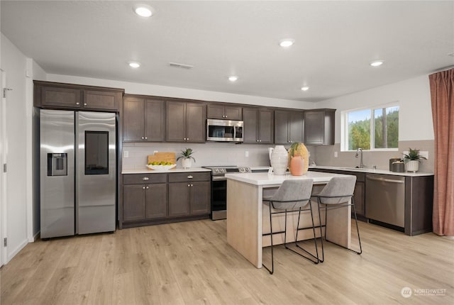 kitchen with a kitchen bar, light wood-type flooring, stainless steel appliances, and a kitchen island