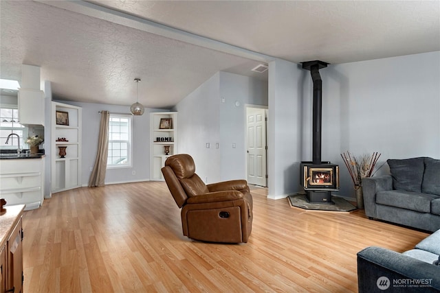 living room featuring sink, a wood stove, a textured ceiling, and light hardwood / wood-style floors