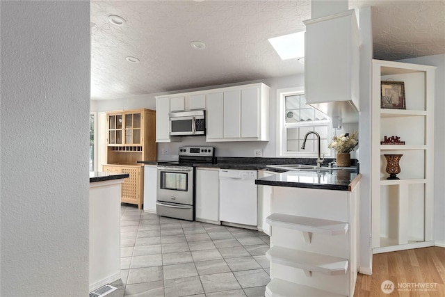 kitchen featuring appliances with stainless steel finishes, a skylight, sink, white cabinets, and a textured ceiling