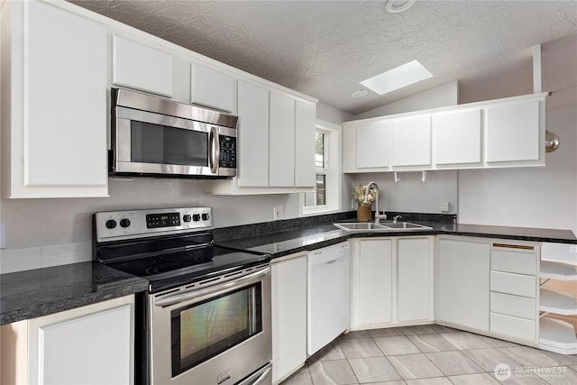 kitchen with lofted ceiling with skylight, sink, light tile patterned floors, stainless steel appliances, and white cabinets