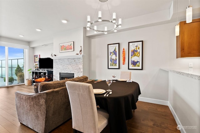 dining room featuring a stone fireplace, recessed lighting, baseboards, dark wood finished floors, and an inviting chandelier