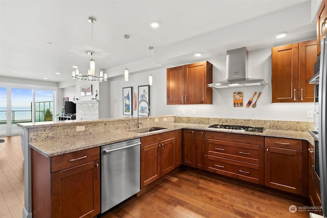 kitchen with pendant lighting, brown cabinets, appliances with stainless steel finishes, a sink, and wall chimney range hood