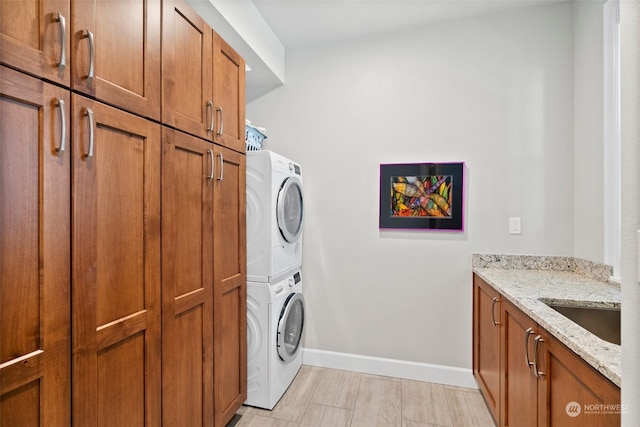 laundry room featuring stacked washer / dryer, cabinet space, a sink, and baseboards