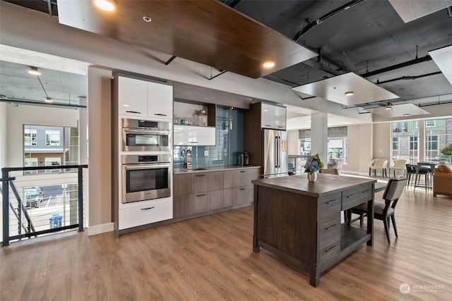 kitchen featuring light wood finished floors, white cabinets, dark countertops, modern cabinets, and appliances with stainless steel finishes