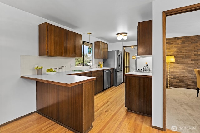 kitchen featuring stainless steel appliances, decorative backsplash, light hardwood / wood-style floors, pendant lighting, and kitchen peninsula