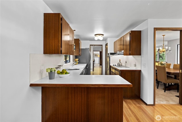 kitchen with kitchen peninsula, stainless steel appliances, light hardwood / wood-style flooring, tasteful backsplash, and pendant lighting