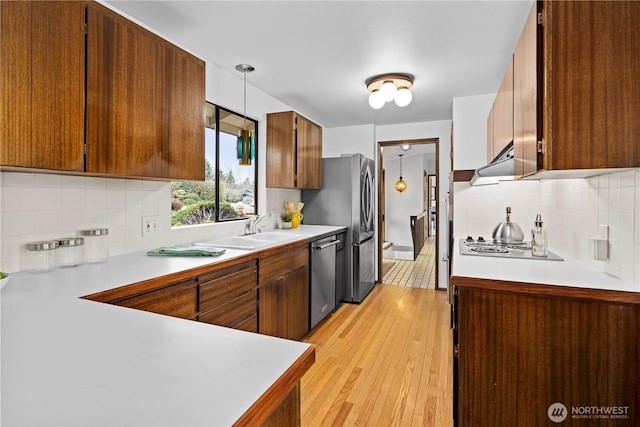 kitchen featuring sink, light wood-type flooring, exhaust hood, decorative light fixtures, and stainless steel appliances