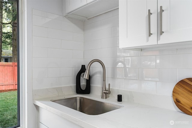 interior details featuring white cabinetry, sink, backsplash, and light stone counters