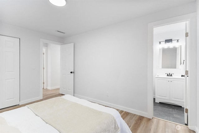 bedroom with ensuite bath, sink, and light hardwood / wood-style flooring