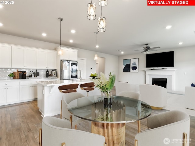 dining room featuring light wood-style flooring, a fireplace, a ceiling fan, and recessed lighting