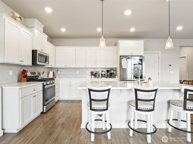 kitchen featuring an island with sink, pendant lighting, stainless steel appliances, and light countertops