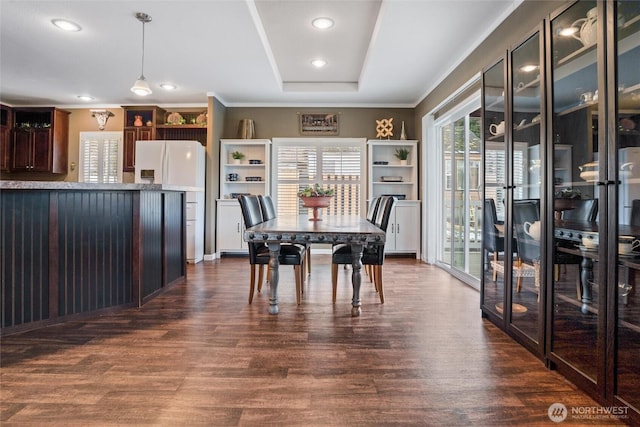 dining room with dark wood-type flooring, ornamental molding, and a tray ceiling