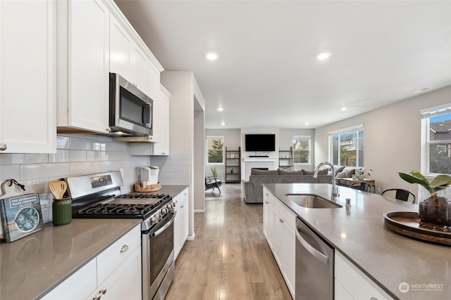 kitchen with appliances with stainless steel finishes, sink, white cabinets, backsplash, and light hardwood / wood-style flooring