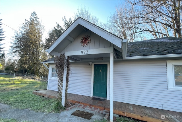 property entrance with roof with shingles, a yard, and fence