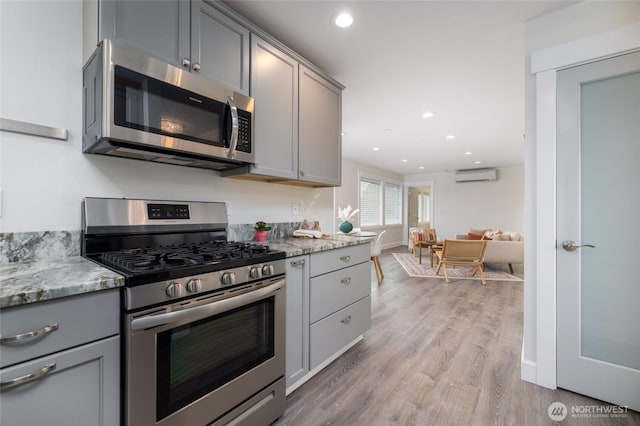 kitchen featuring light stone countertops, gray cabinetry, stainless steel appliances, and a wall mounted air conditioner