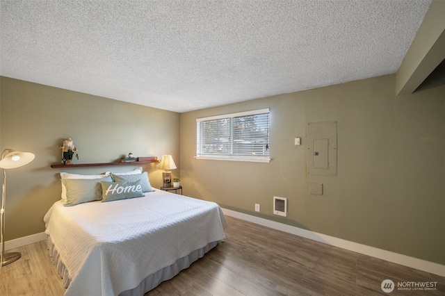 bedroom with hardwood / wood-style floors, electric panel, and a textured ceiling