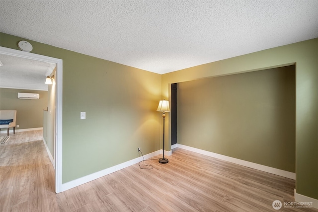 unfurnished room featuring a wall mounted AC, light hardwood / wood-style flooring, and a textured ceiling