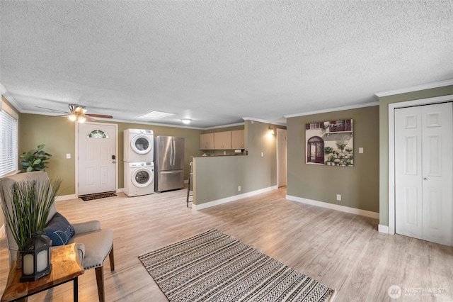 living room with stacked washing maching and dryer, ornamental molding, ceiling fan, light hardwood / wood-style floors, and a textured ceiling