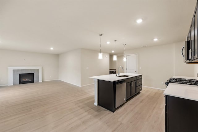 kitchen with sink, hanging light fixtures, light hardwood / wood-style flooring, an island with sink, and stainless steel appliances