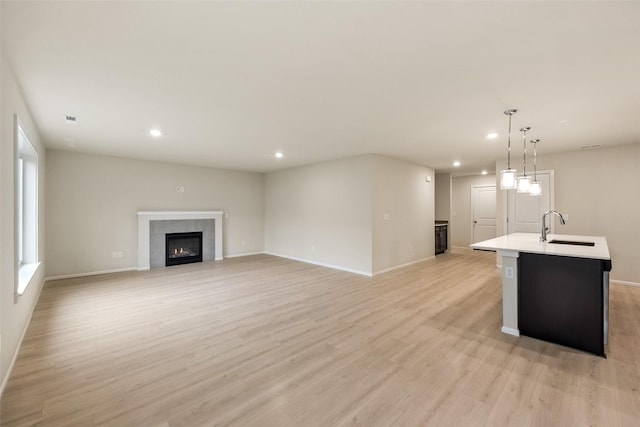 unfurnished living room with a tiled fireplace, sink, and light wood-type flooring