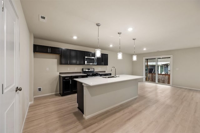 kitchen with appliances with stainless steel finishes, sink, hanging light fixtures, a center island with sink, and light hardwood / wood-style flooring