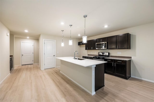 kitchen with sink, decorative light fixtures, light hardwood / wood-style flooring, stainless steel appliances, and a kitchen island with sink