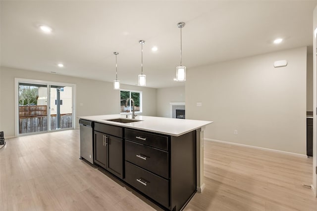 kitchen featuring decorative light fixtures, sink, a kitchen island with sink, stainless steel dishwasher, and light wood-type flooring