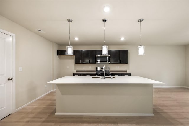 kitchen with appliances with stainless steel finishes, hanging light fixtures, a center island with sink, and light hardwood / wood-style flooring