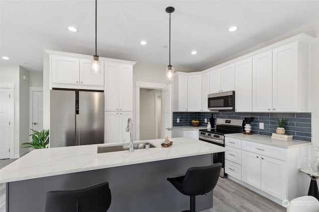 kitchen featuring pendant lighting, sink, stainless steel appliances, white cabinets, and a center island with sink