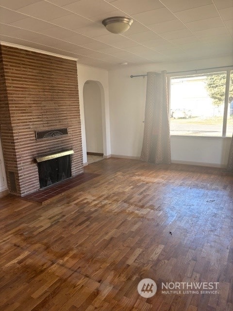 unfurnished living room featuring a brick fireplace and dark wood-type flooring