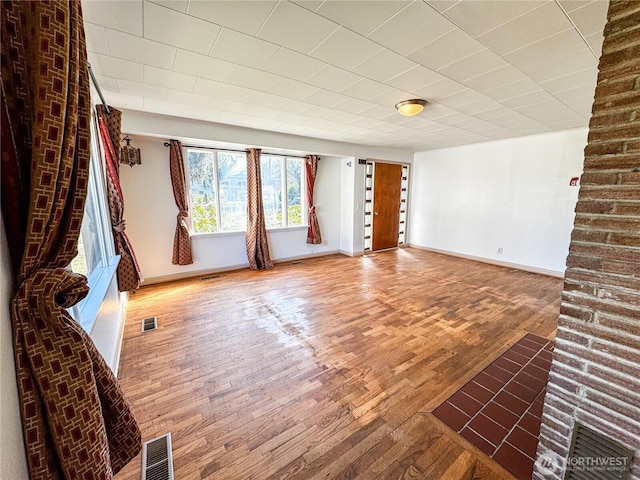 unfurnished living room with wood finished floors, visible vents, and baseboards