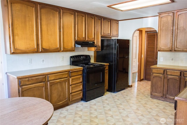 kitchen with arched walkways, light floors, light countertops, under cabinet range hood, and black appliances