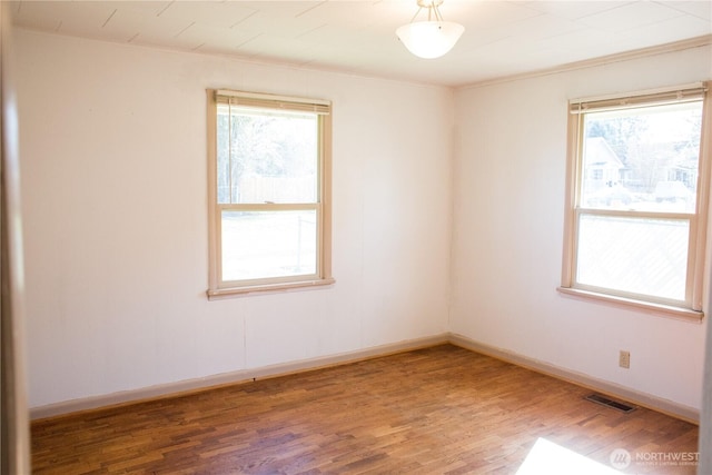 unfurnished room featuring a wealth of natural light, visible vents, baseboards, and wood finished floors