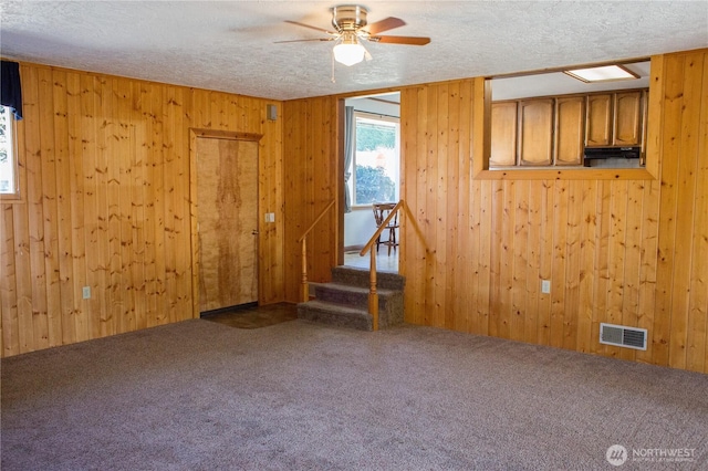 empty room featuring wooden walls, carpet flooring, visible vents, and a textured ceiling